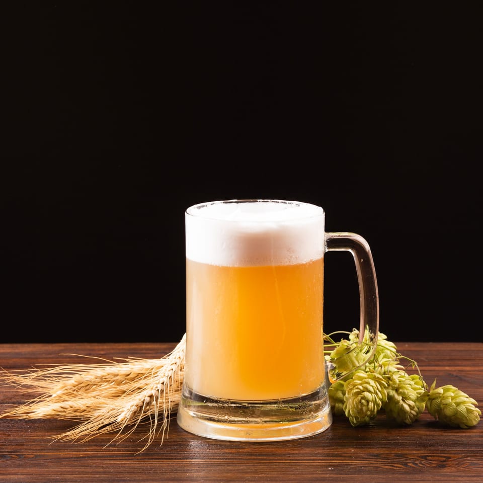 A frothy mug of Big Oven Pizza's golden beer, with wheat and hops on a wooden table.