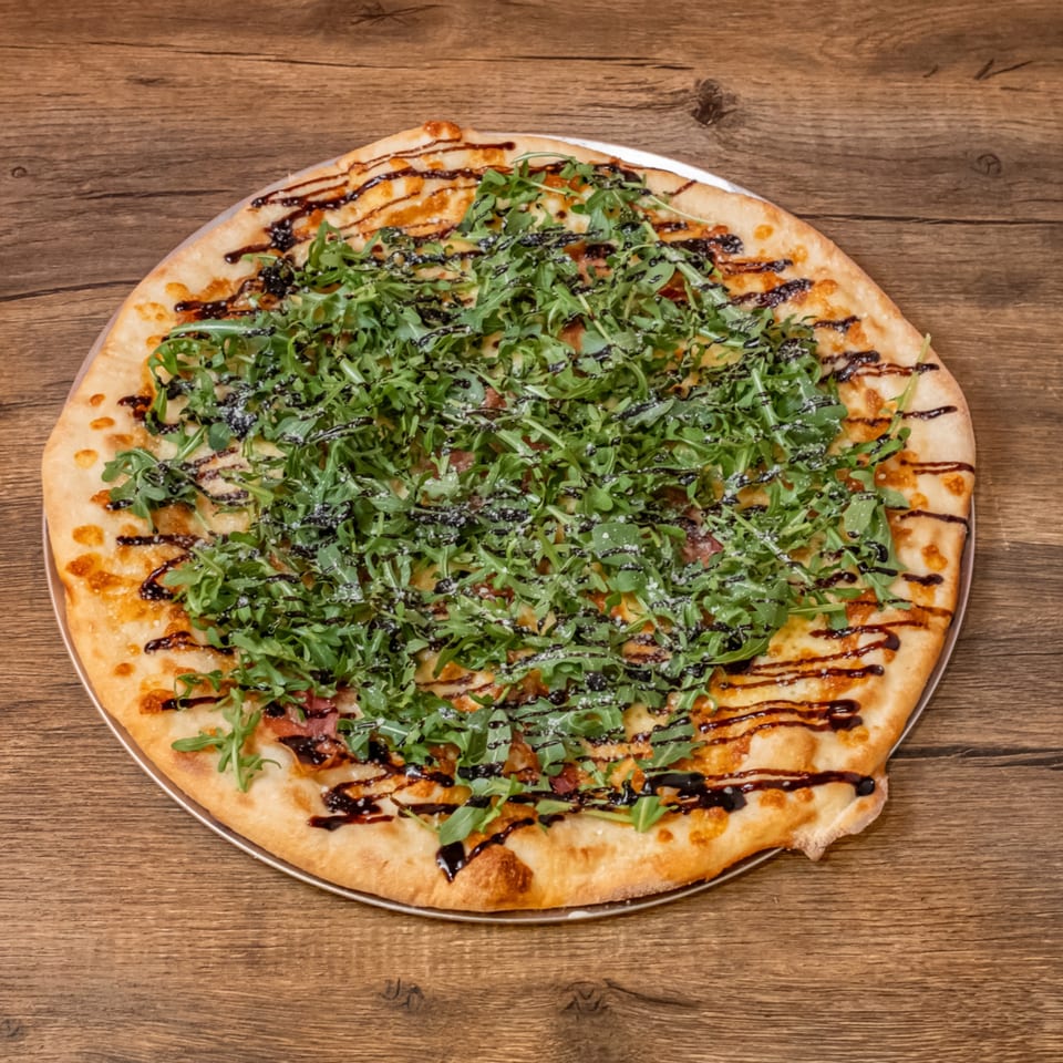 Big Oven Pizza's arugula and balsamic glaze pizza, topped with parmesan, on a wooden table.