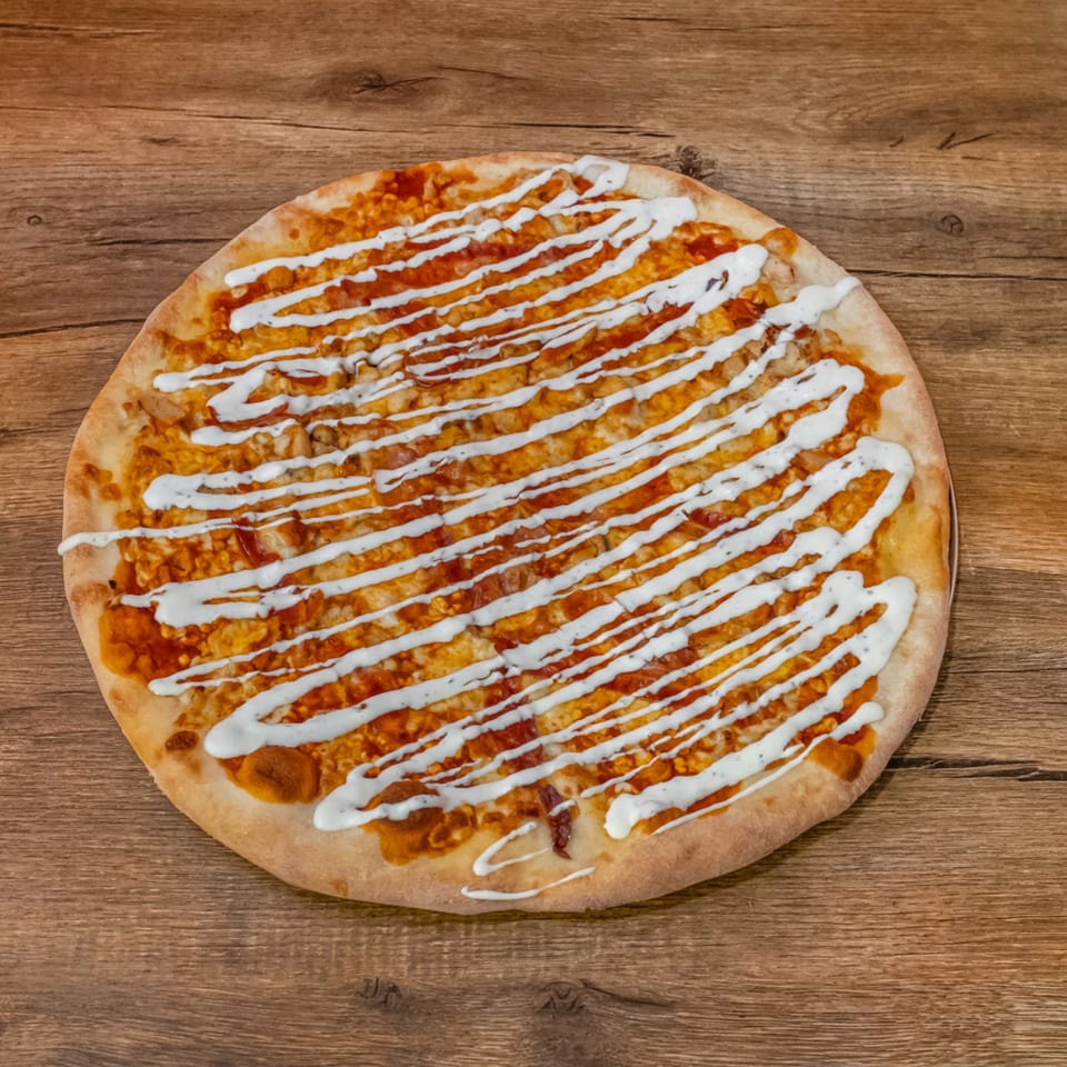 Big Oven Pizza's Buffalo Chicken Pizza with white ranch drizzle on a wooden table.