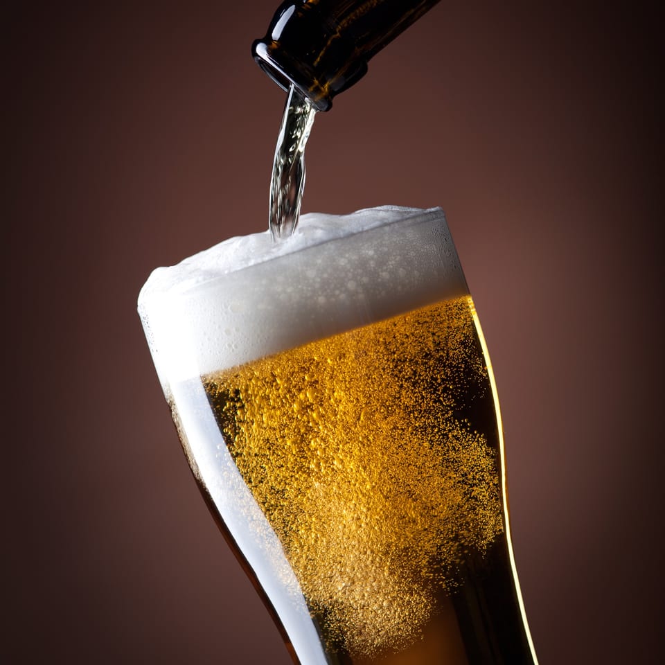 Beer pouring from a bottle into a glass, creating a foamy head and many bubbles.