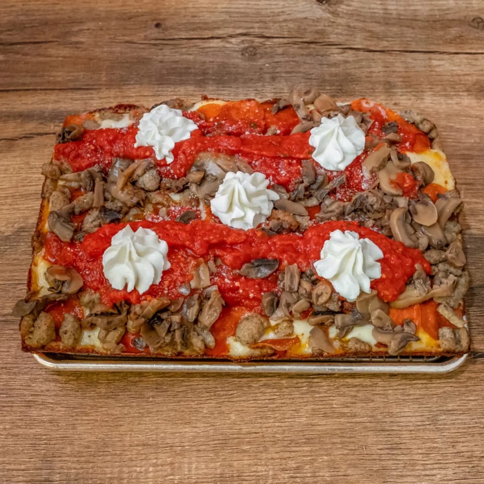 A rectangular Big Oven Pizza with red sauce stripes, mushrooms, sausage, and dollops of white ricotta.